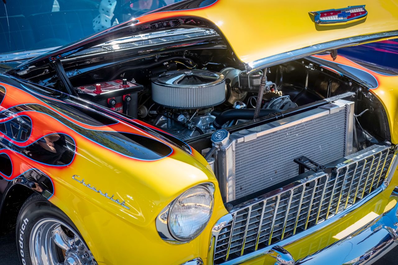 Close-up of a vintage Chevrolet car with hood open, showcasing its engine and vibrant flame livery.