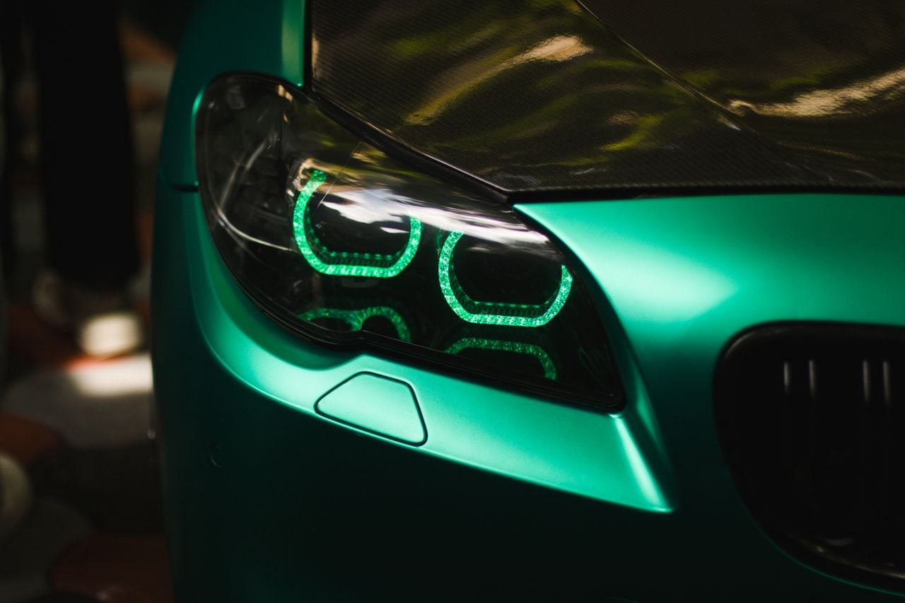 Close-up of a green sports car headlight, showcasing futuristic LED design and sleek bodywork.