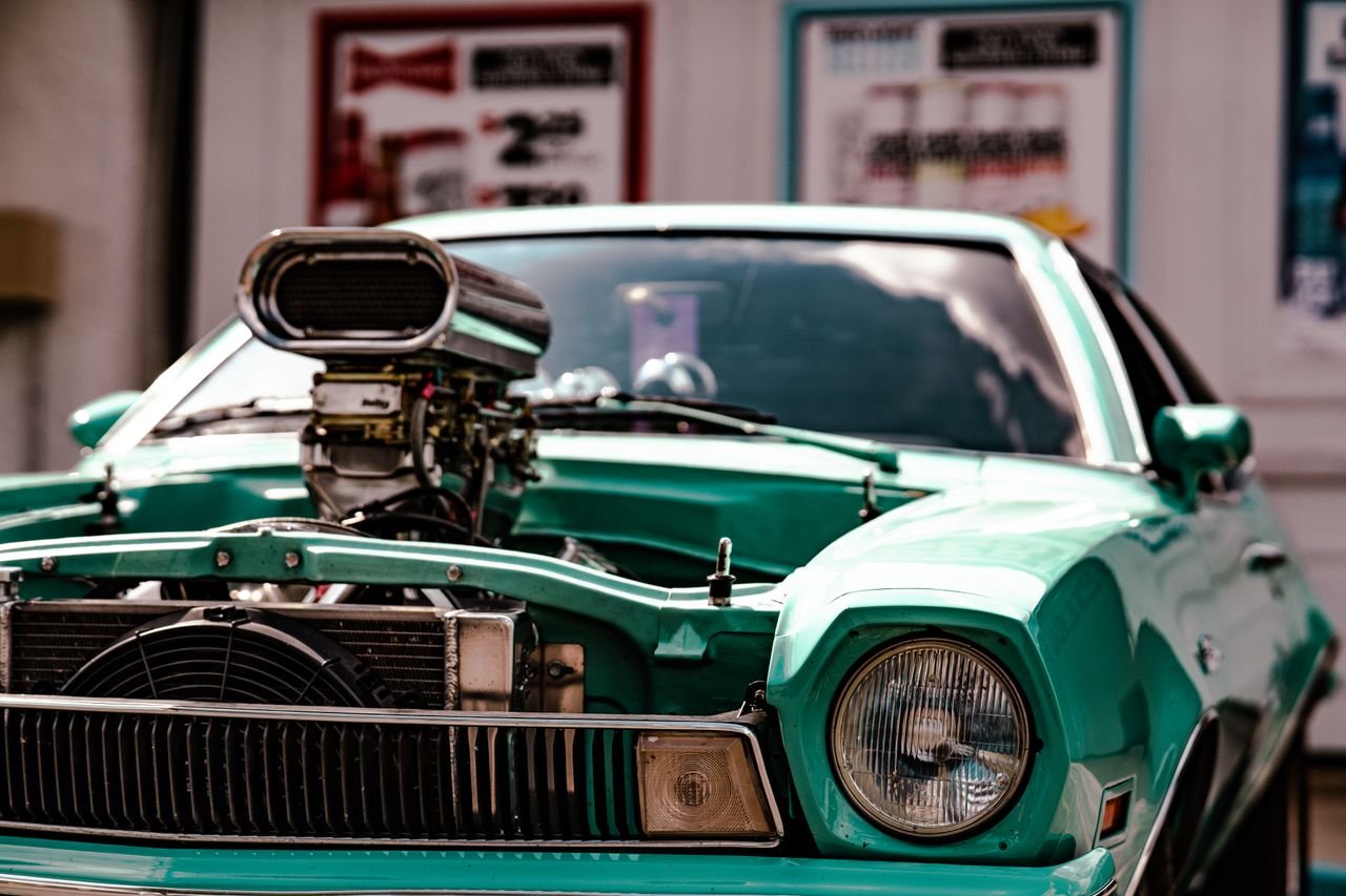 Close-up of a vintage muscle car showcasing a powerful supercharger in a vibrant setting.